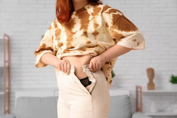 Image of woman trying to do her trousers up after pregnancy weight gain York
